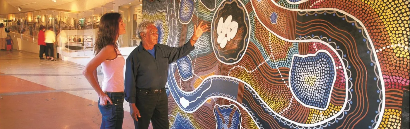 A guide points out details of a large Aboriginal dot-painting mural to a visitor inside Kodja Place, Kojonup