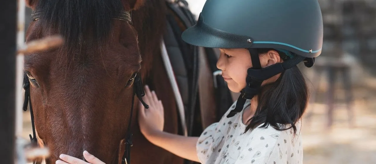A young girl in a riding helmet gently petting a horse at a country show